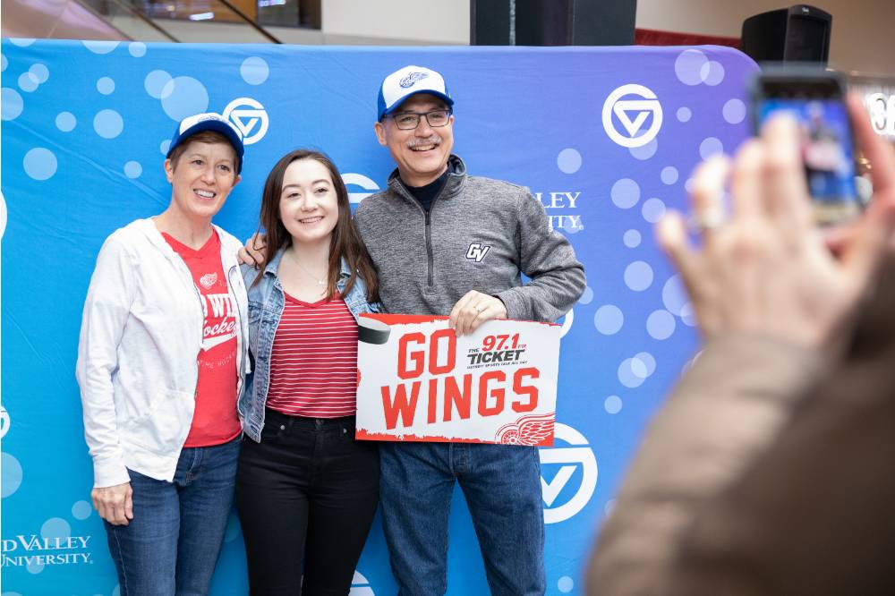 Three alumni pose together with a "Go Wings" sign at the Detroit Red Wings GVSU Night